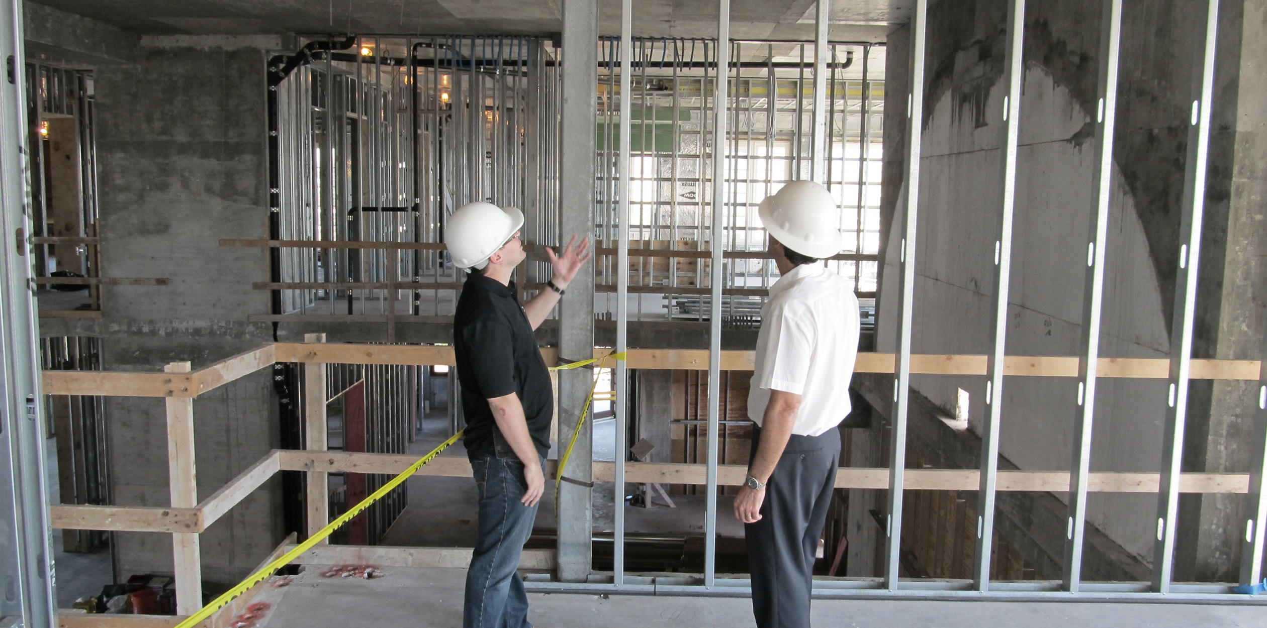 Builder and technology integrator reviewing open stud framing to plan low-voltage wiring before drywall