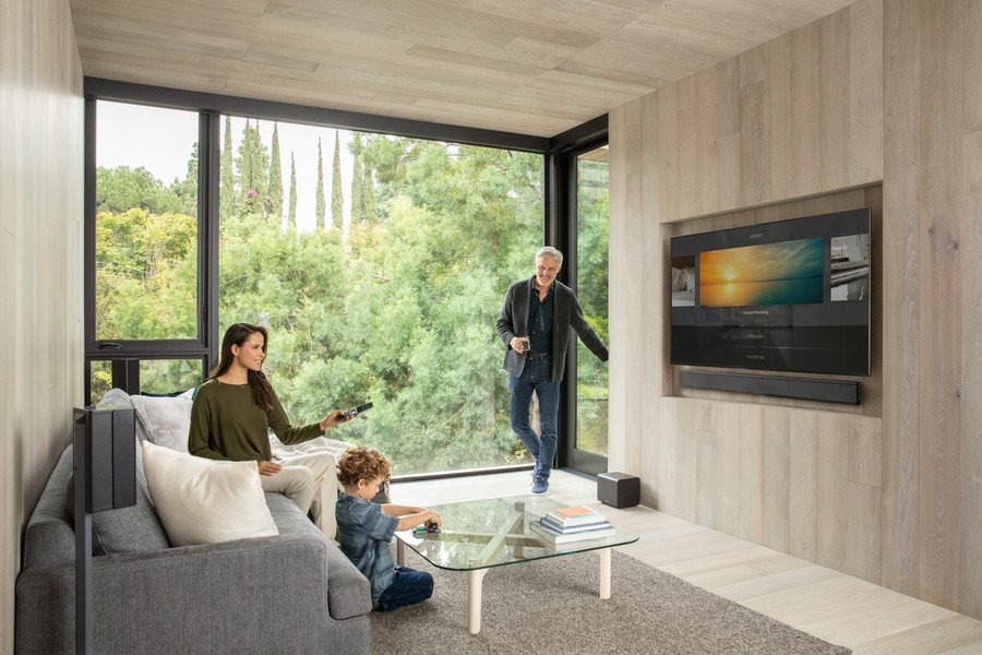 a family in a living room with a glass window and a wall-mounted TV