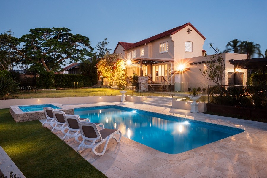 Luxury home in the early evening as seen across a perfectly blue pool and smart stonework. 