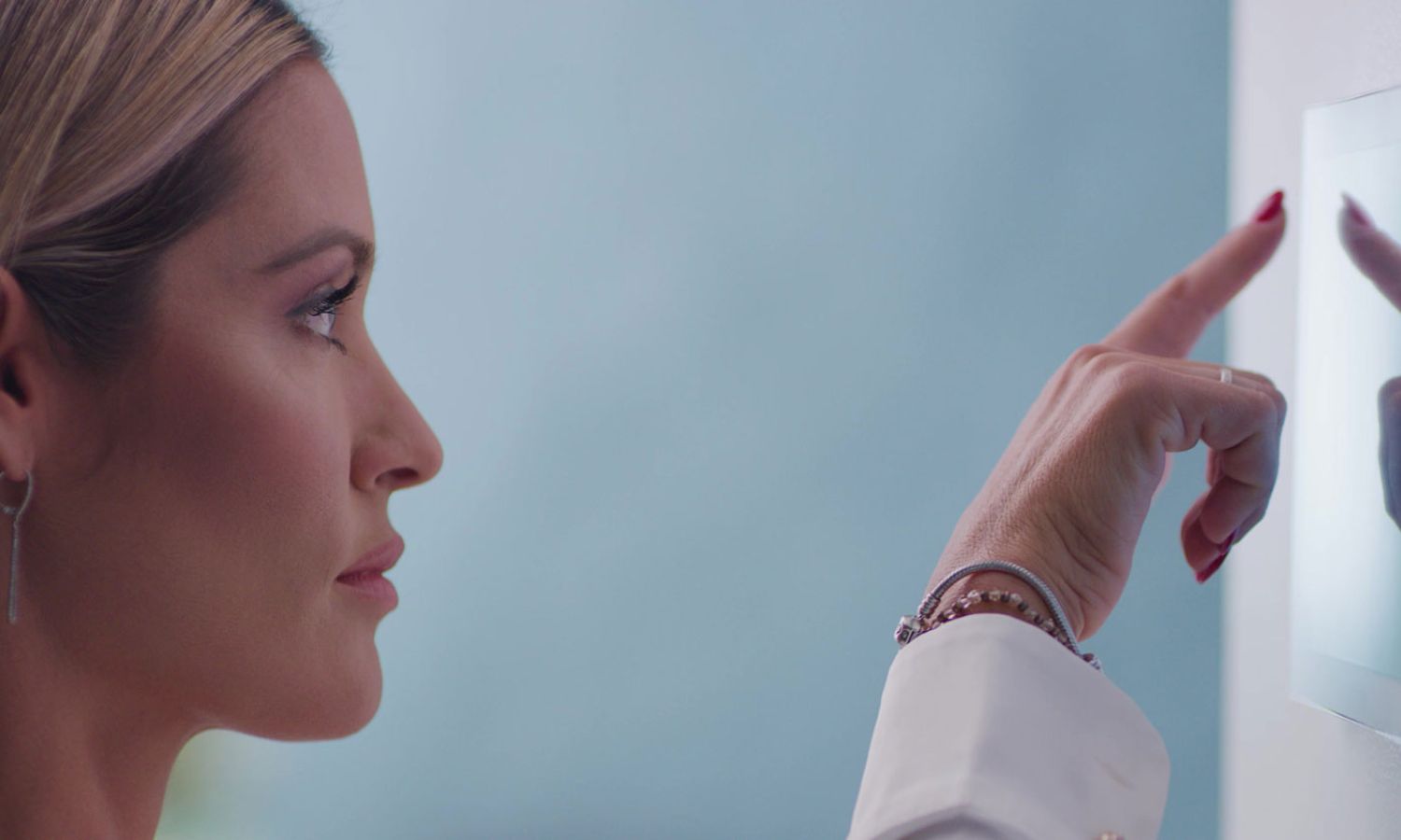 Close‑up of a person reaching toward a wall‑mounted touchscreen panel in a softly lit modern space.